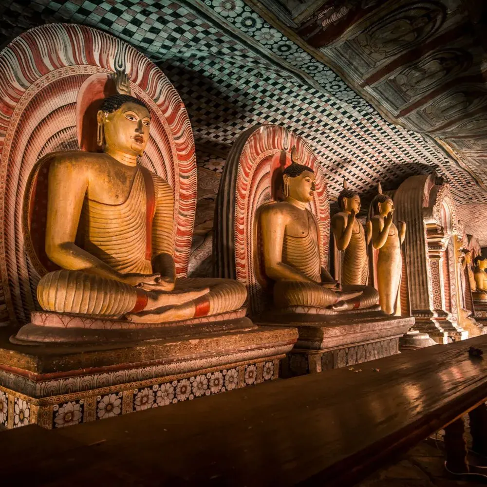 Rows of seated Buddha statues and painted ceilings inside the Dambulla cave temple