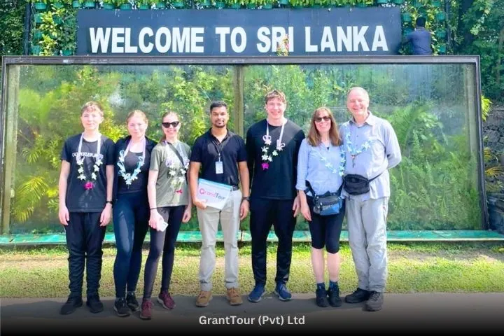 Six travellers in flower garlands with their GrandTour guide under a &ldquo;Welcome to Sri Lanka&rdquo; sign