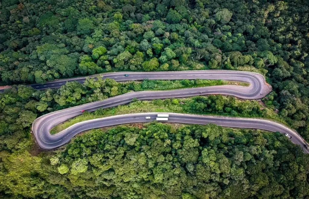 A road winding in tight curves through dense forested hills, seen from above