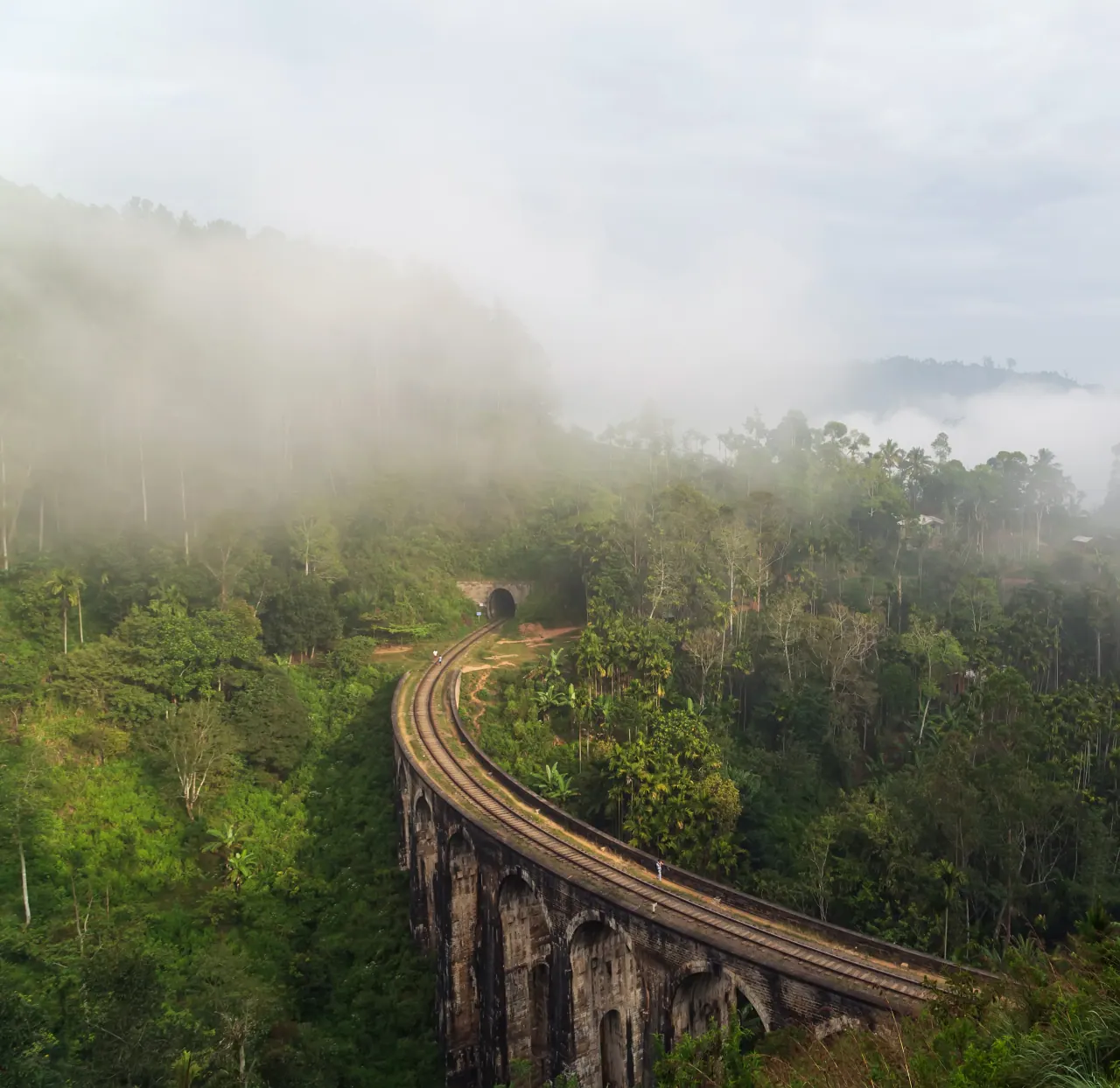 The Nine Arches Bridge curving through misty jungle near Ella, its rails vanishing into a tunnel